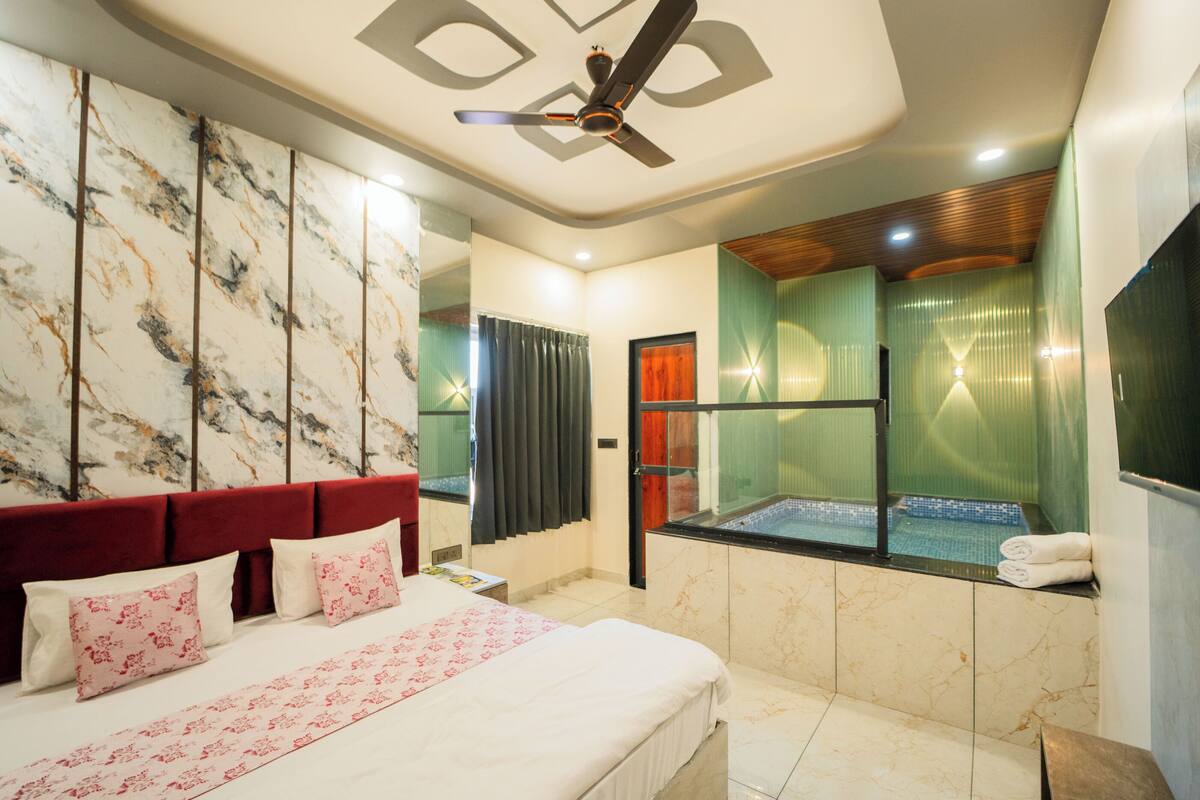 A hotel room with a bed, a ceiling fan, a bathtub, and a large mirror.