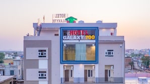 A multi-story hotel with balconies, a prominent sign reading 'HOTEL GALAXY 700,' and a parking area with cars.