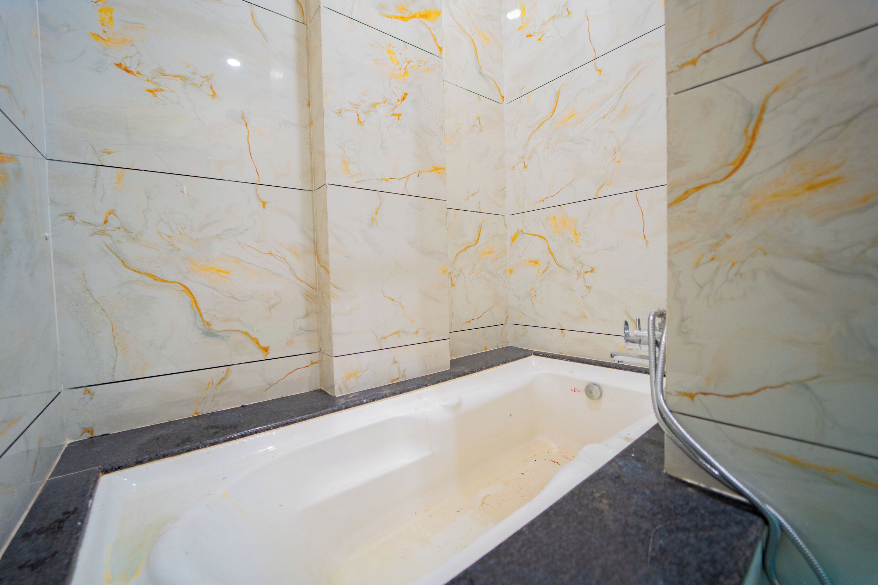 Un baño con bañera, paredes de mármol y encimera negra.