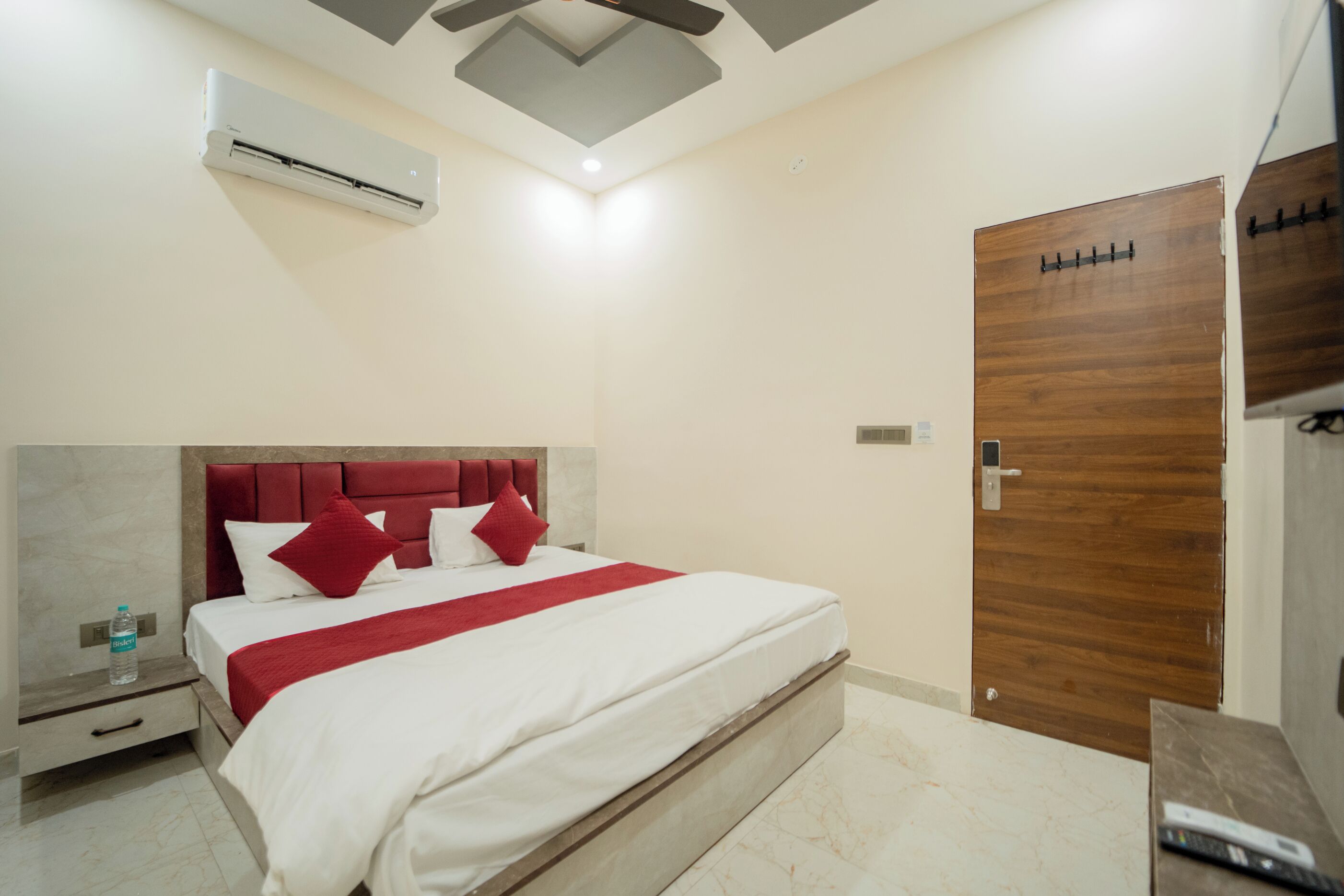 Una habitación de hotel con cama, puerta de madera, mesita de noche y equipo de aire acondicionado.