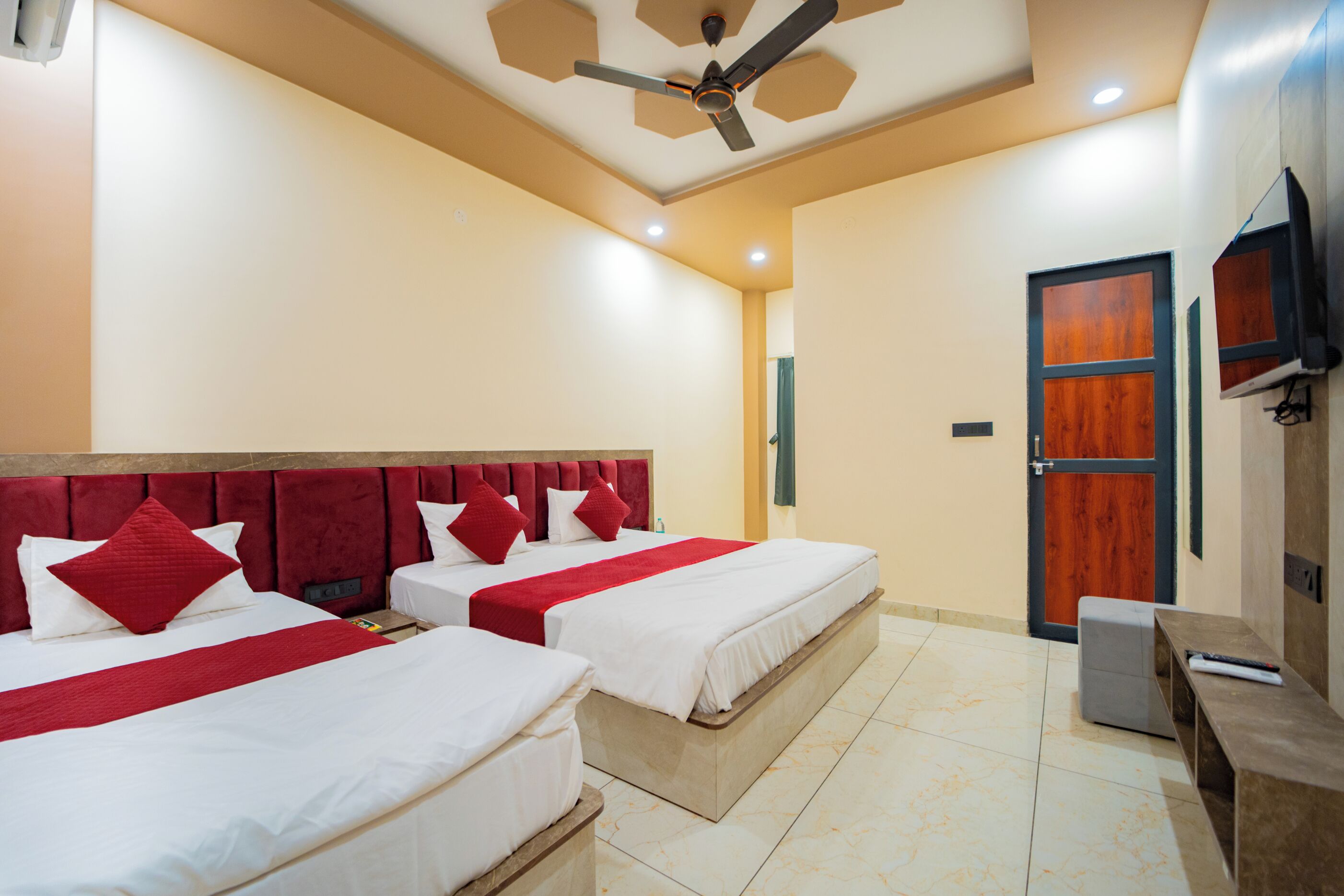 A hotel room with two beds, a ceiling fan, a wooden door, and a television on the wall.