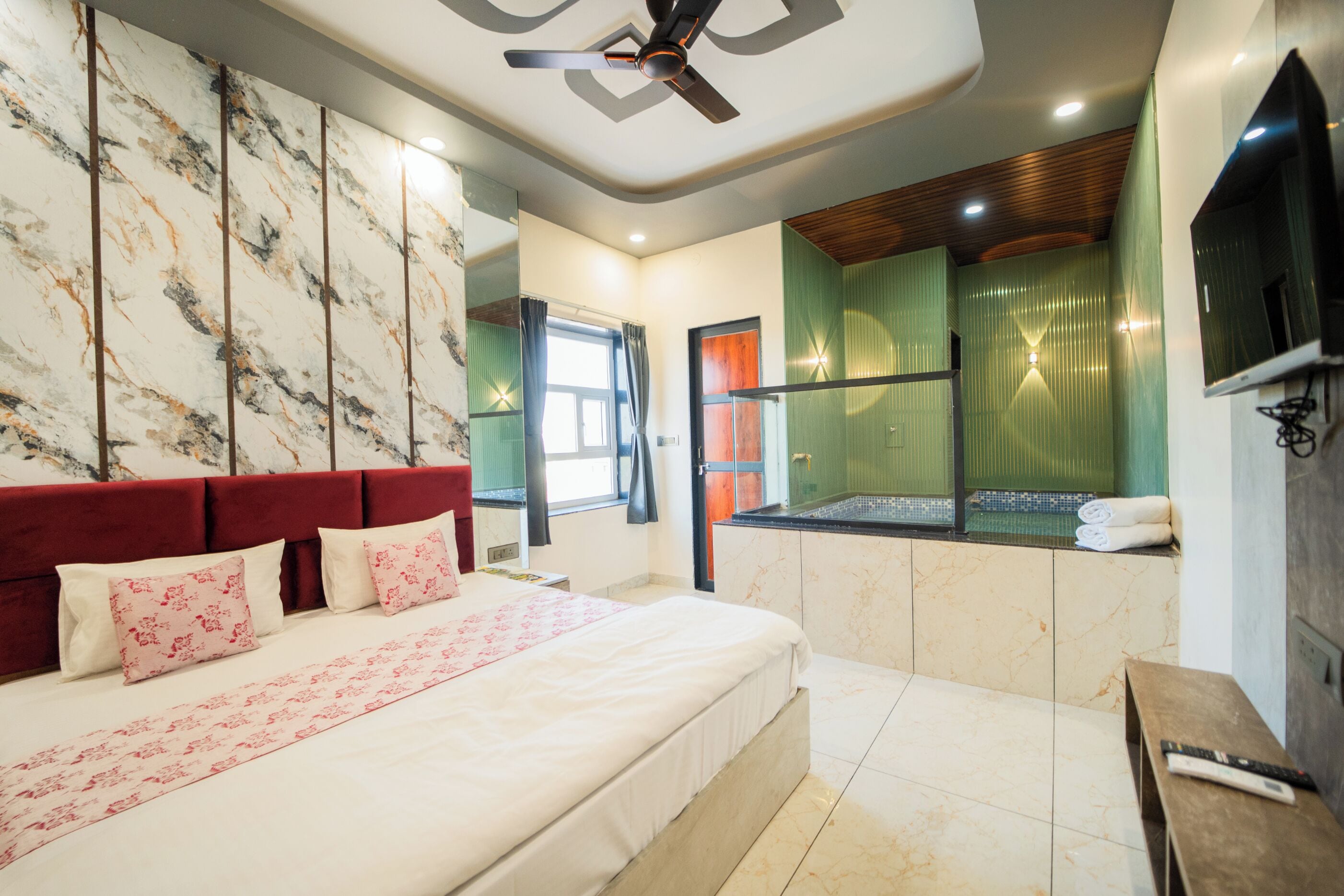 A modern hotel room with a large bed, a TV, a ceiling fan, and a view of the outside.