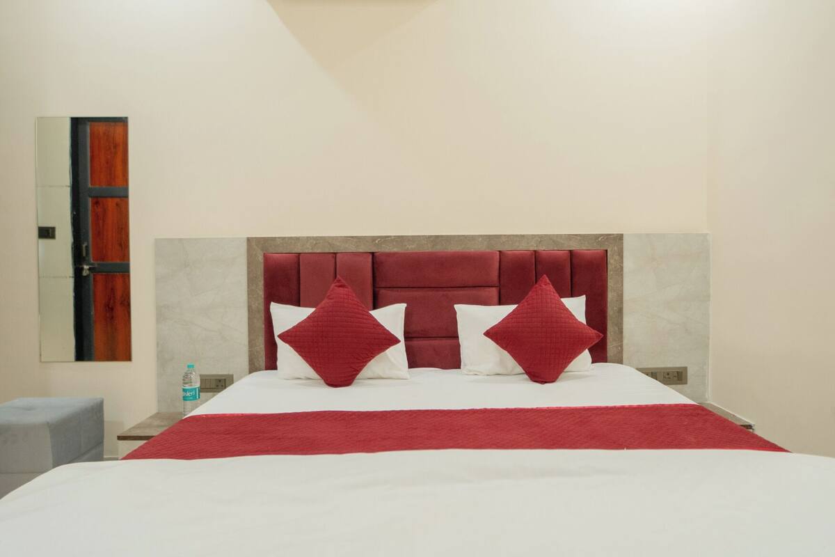 A hotel room with a large bed, a red headboard, and a small bedside table with a bottle.