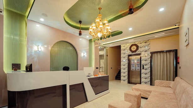 A hotel reception area with a reception desk, a chandelier, a sofa, and an elevator.