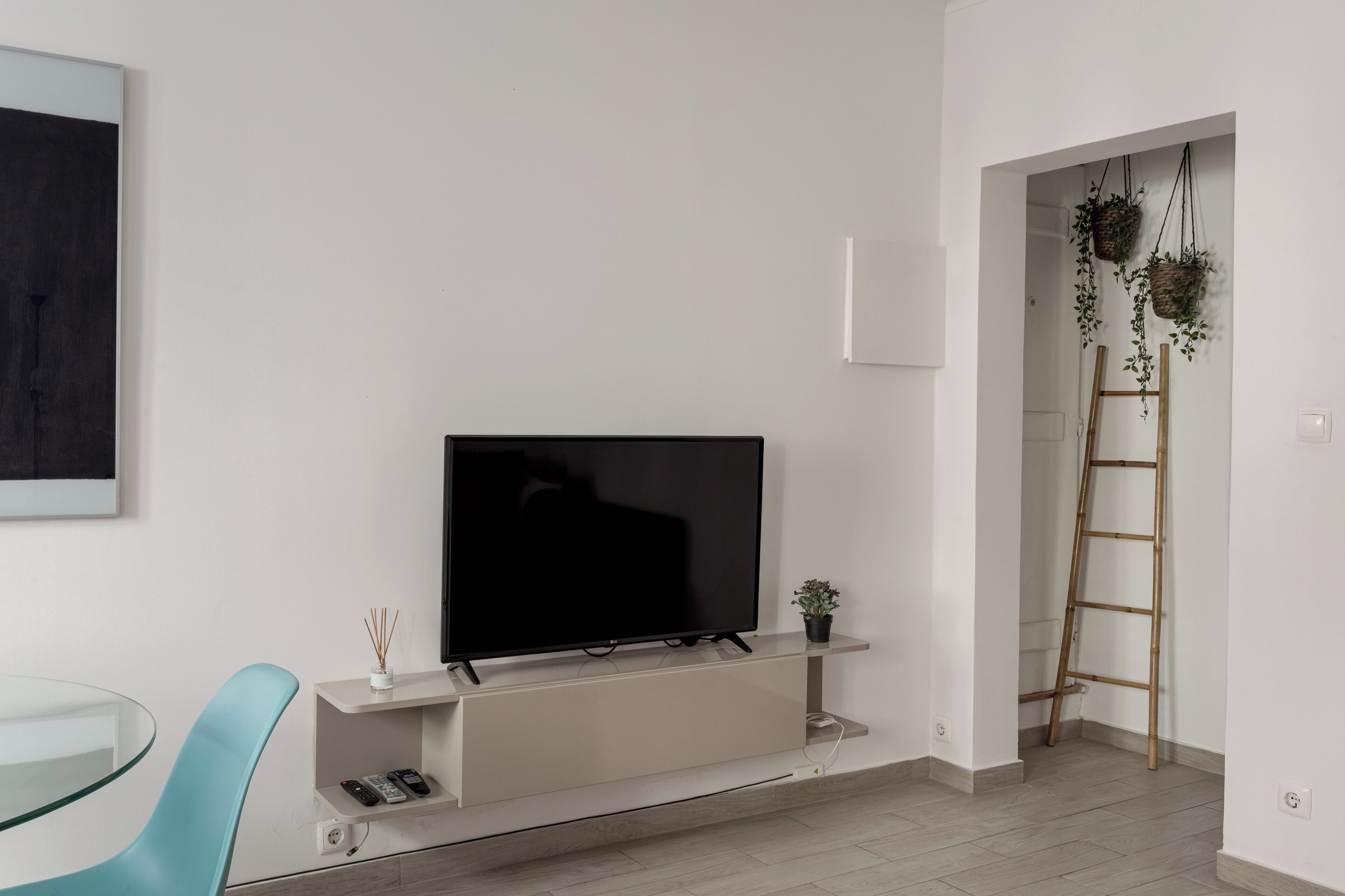 Ein modernes Wohnzimmer mit Flachbildfernseher in einer Wandnische, einem Glastisch und einem stuhl in Türkis sowie einer Leiter in der Ecke.