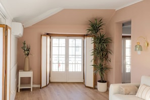 A room with a wooden floor, a white sofa, a potted plant, and a door with glass panels. - Sea View Alfama Nest – 1BR Apartment (Lisbon)