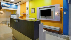 A reception desk with a flat-screen TV, a clock, and a whiteboard in a brightly colored room with a tiled floor. - Hotel O near Terminal Batoh formerly (Banda Aceh)