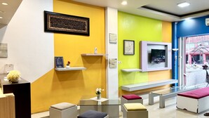 A modern waiting area with a yellow and green wall, a mounted TV, and a reception desk. - Hotel O near Terminal Batoh formerly (Banda Aceh)