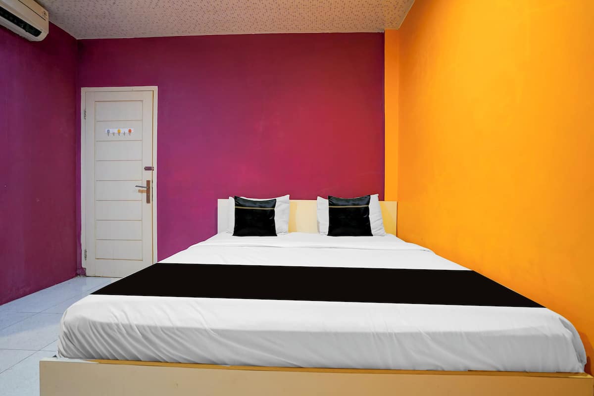Una cama con ropa de cama blanca y almohadas negras, una puerta blanca y una pared con degradado de morado a naranja.