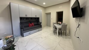 Un espace de vie compact comprenant un canapé, une table à manger et un téléviseur fixé au mur.