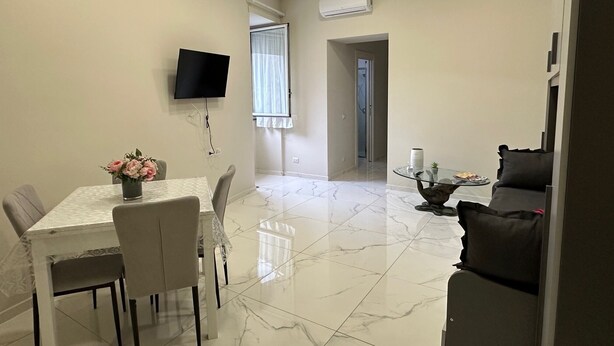 Un salon moderne comprenant un coin repas, un téléviseur à écran plat fixé au mur et une grande fenêtre avec des rideaux.