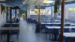 En udendørs café med borde og stole placeret under et overdækket område, samt en hængekøje.