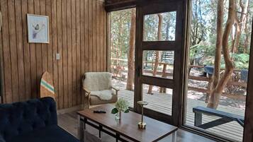 Una habitación con pared de madera, una silla blanca, un sofá azul y una mesa de madera con un jarrón y un control remoto.