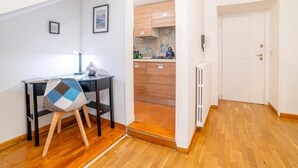 Ein kompakter Wohnbereich mit Holzboden, einem kleinen Essbereich mit Tisch und Stuhl, einer Küche mit Holzausstattung und einer weißen Tür.