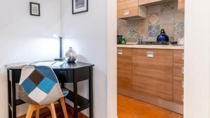Ein kompakter Raum mit einem Holztisch und Stuhl, einer kleinen Küchenzeile mit Holzschränken und einem Fliesenboden.