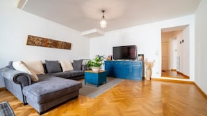Ein Wohnzimmer mit grauem Sofa, blauem Schrank und Fernseher.