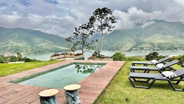 Una zona de piscina con terraza de madera, dos mesas redondas y sillones de descanso.