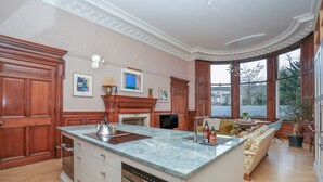 A spacious kitchen with a marble island, wooden cabinets, and a fireplace. - Luxury Flat Overlooking Eglinton Gardens (Edinburgh)