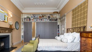 A bedroom with a bed, a green armchair, a wooden dresser, a fireplace, and a bookshelf. - Luxury Flat Overlooking Eglinton Gardens (Edinburgh)