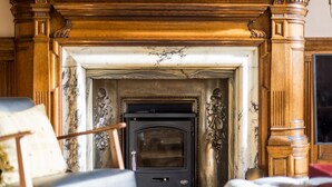A fireplace with intricate woodwork and a mantel, flanked by two chairs. - Luxury Flat Overlooking Eglinton Gardens (Edinburgh)