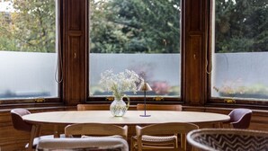 A round dining table with a vase of flowers, wooden chairs, and a view through a frosted window. - Luxury Flat Overlooking Eglinton Gardens (Edinburgh)