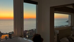 Una habitación con una bañera grande, una cama y vistas al mar al atardecer.