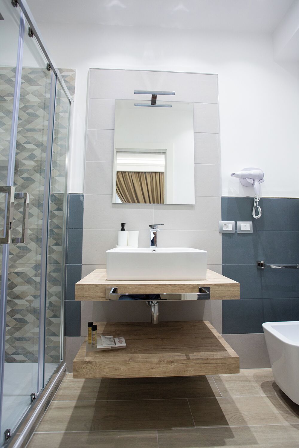 A modern bathroom with a glass shower enclosure, a white sink with a mirror above, and a white bathtub.