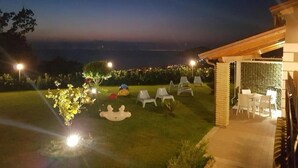 Vista nocturna de un patio trasero con zona de estar al aire libre y un jardín bien iluminado.