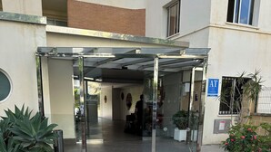 Hotellin sisäänkäynti, jossa on lasiovi, opastekyltti, joka osoittaa parkkialueen, ja ruukussa oleva kasvi.