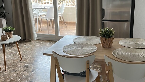 Moderni keittiö, jossa on sisäänrakennettu jääkaappi, kattotuuletin ja ruokailutila, jossa on pöytä kahdelle.