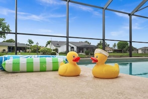A poolside area with two rubber ducks and a green and white inflatable pool float. - Sunny Cape Escape (Cape Coral)