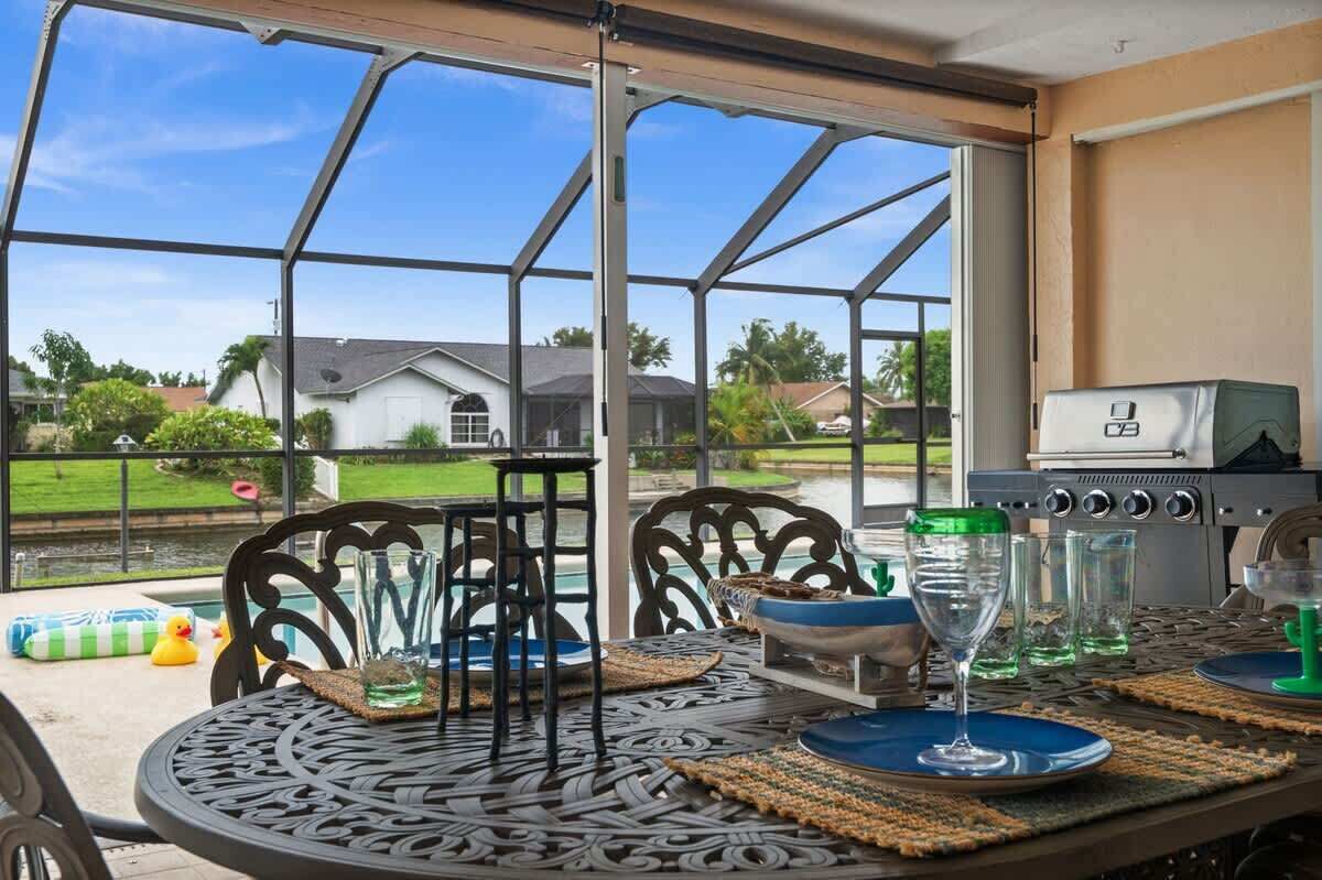 A covered patio with a table set for dining, a grill, and a view of a residential area.