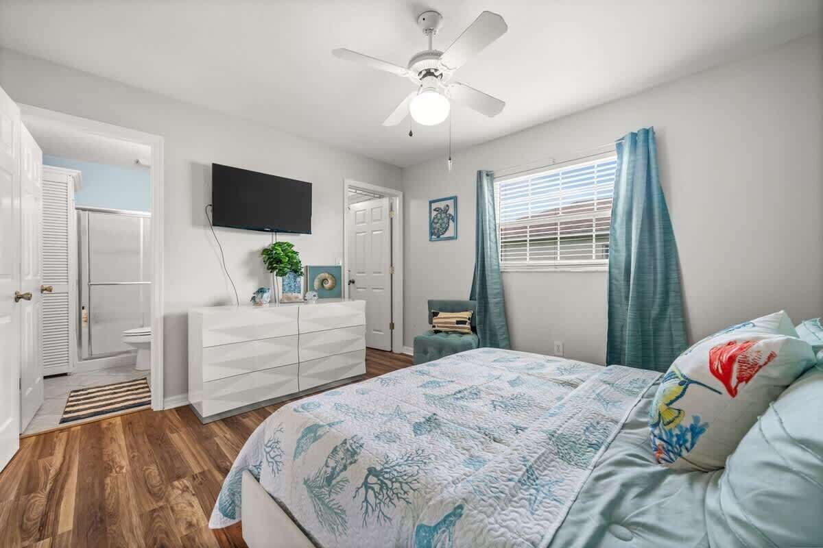 A bedroom with a bed, a ceiling fan, a television, and a window with curtains.