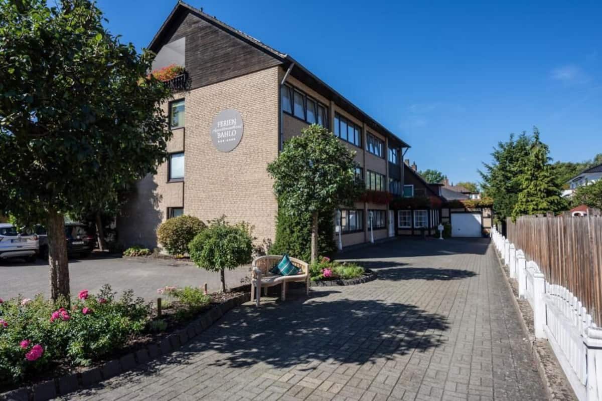 A building with a sign reading 'FERIENBAHLO' and a paved driveway with a bench and flower beds.