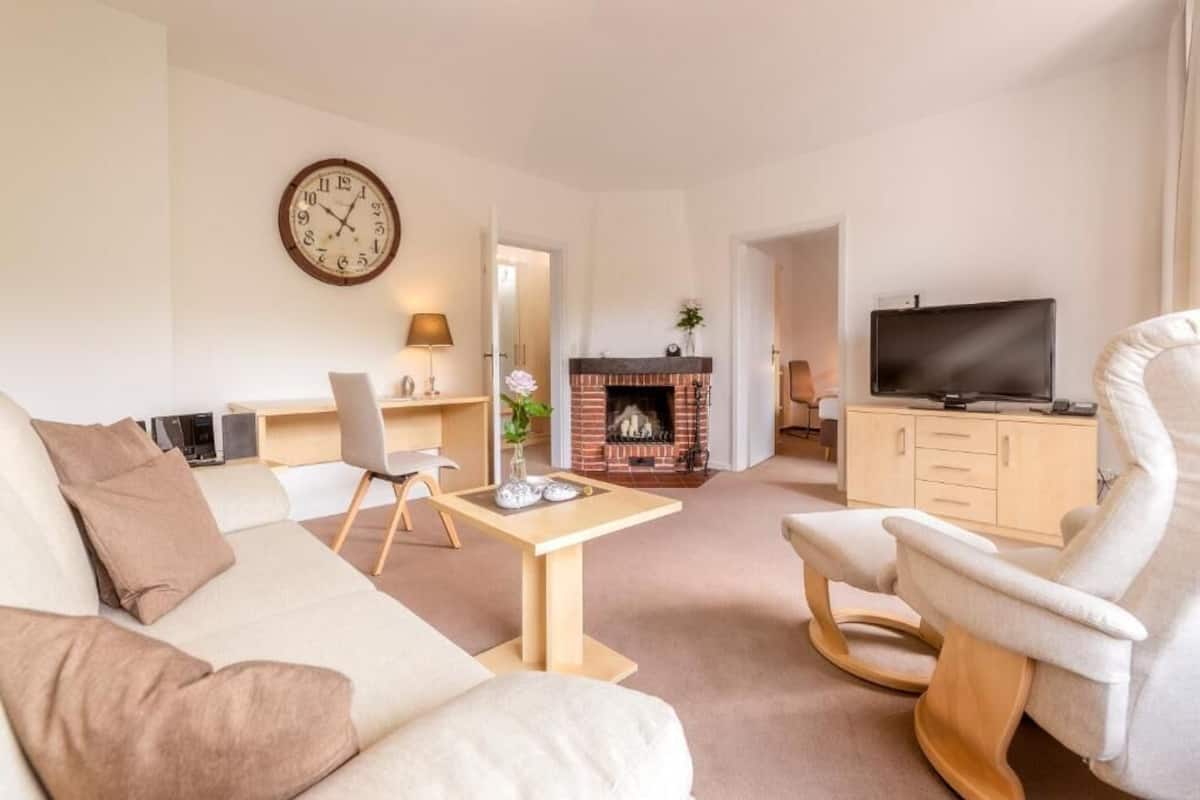 A living room with a sofa, a TV, a fireplace, a clock, and a desk with a lamp.