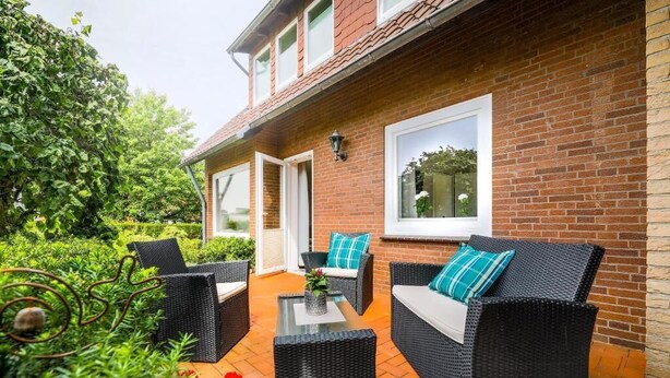 A patio with wicker furniture, a glass table, and a brick wall. - Appartementhaus Bahlo (Bad Bevensen)