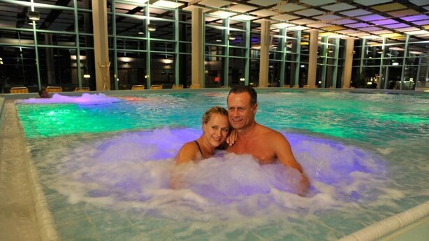 Un couple dans un jacuzzi, avec vue sur un grand espace intérieur aux murs de verre.