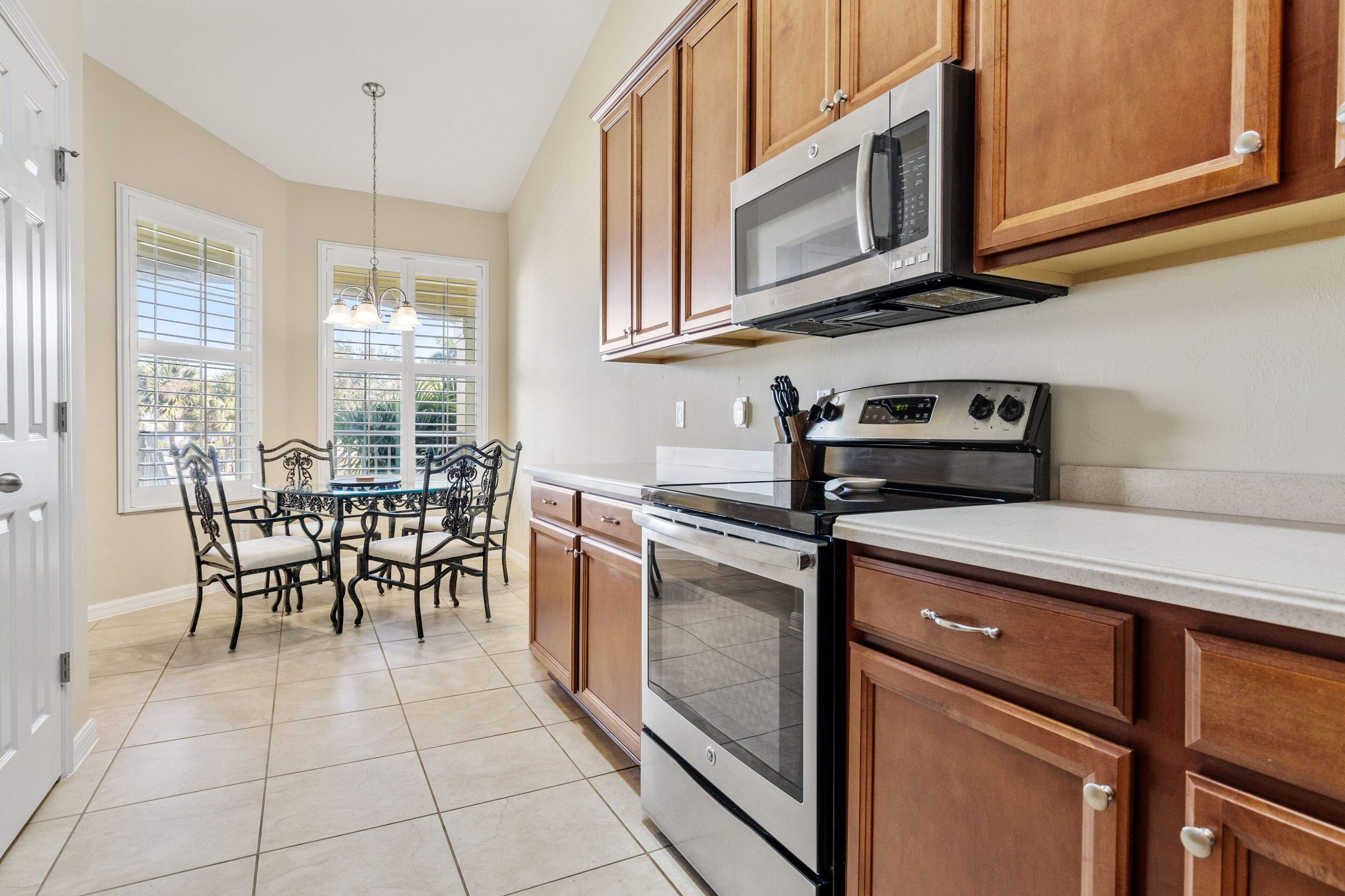 A kitchen with wooden cabinets, a microwave, an oven, a dining table with chairs, and a chandelier.