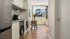 A modern kitchen with stainless steel appliances, a washing machine, and a dining area with a view of the cityscape. - Dolce Vita | Modern Sea Point Retreat (Cape Town)