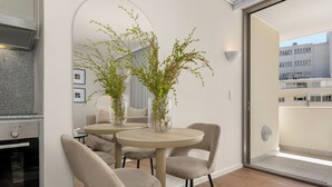 A modern kitchen with a built-in oven, a dining area with two round tables and chairs, and a large window offering a view of a building. - Dolce Vita | Modern Sea Point Retreat (Cape Town)