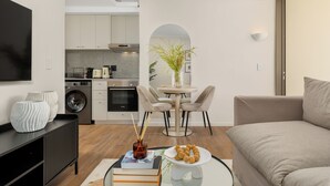 A modern living room with a sofa, a dining table with chairs, a kitchen area with appliances, and a TV mounted on the wall. - Dolce Vita | Modern Sea Point Retreat (Cape Town)
