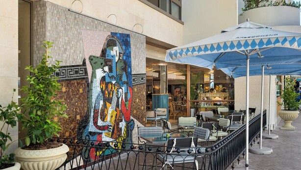 An outdoor seating area with tables and chairs, a large mural on the wall, and a decorative plant. - Dolce Vita | Modern Sea Point Retreat (Cape Town)