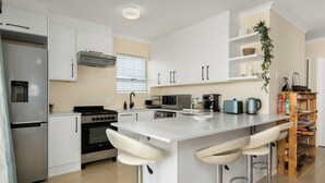Une cuisine moderne avec des meubles blancs, un réfrigérateur en acier inoxydable, une cuisinière à gaz et un grand îlot central doté de tabourets de bar.