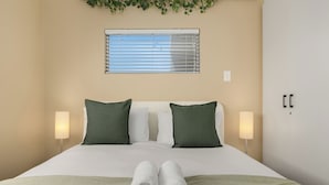 Un lit bien fait, avec des oreillers verts, du linge de lit blanc et deux serviettes enroulées posées sur un plaid vert.