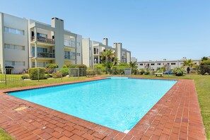 Piscina rectangular con borde de ladrillo, rodeada por una valla y follaje.