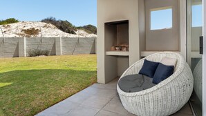 Un espace extérieur moderne aménagé avec des sièges, comprenant une chaise en osier et une petite table, offrant une vue dégagée sur le paysage environnant, et un mur de pierre en arrière-plan.