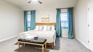 Ein Schlafzimmer mit Bett, einer Bank, einem Deckenventilator und einem Fenster mit Vorhängen.
