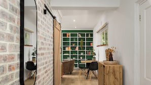 A narrow hallway with a brick wall, a wooden cabinet, and a green shelving unit with books and decorative items. - Serene Green Point Stay |Quiet, Walkable and Central (Cape Town)