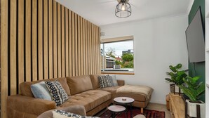 A modern living room with a sectional sofa, a round coffee table, and a wooden accent wall. - Serene Green Point Stay |Quiet, Walkable and Central (Cape Town)