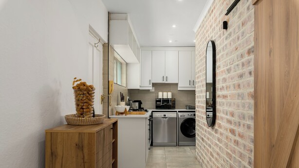 A modern kitchen with white cabinets, a brick wall, and stainless steel appliances. - Serene Green Point Stay |Quiet, Walkable and Central (Cape Town)